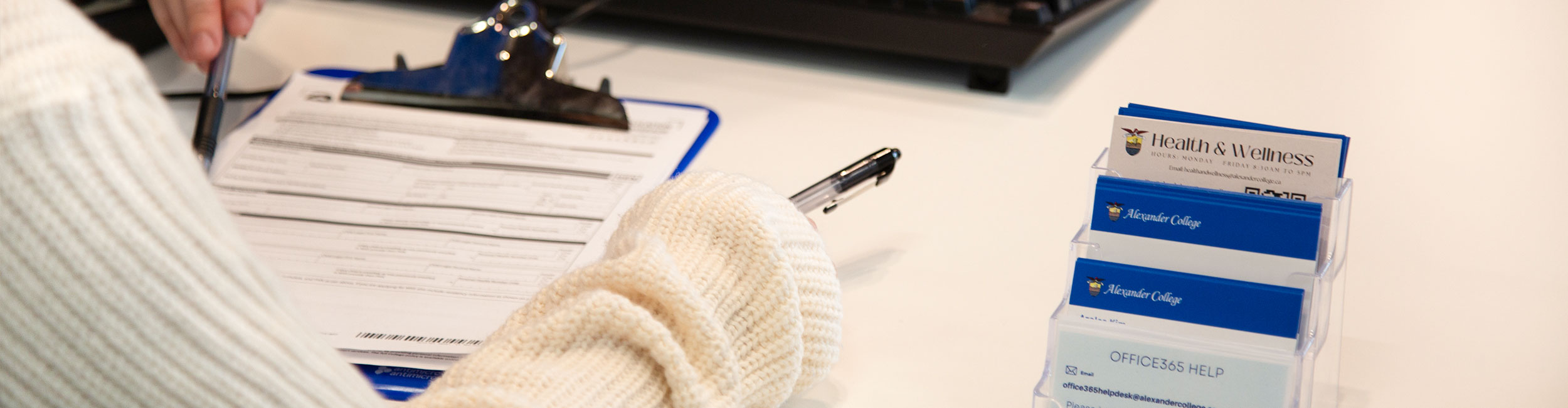 A close up shot of a business card holder containing cards of various departments and a clipboard with a form