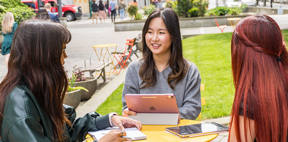 three students studing at a table outside