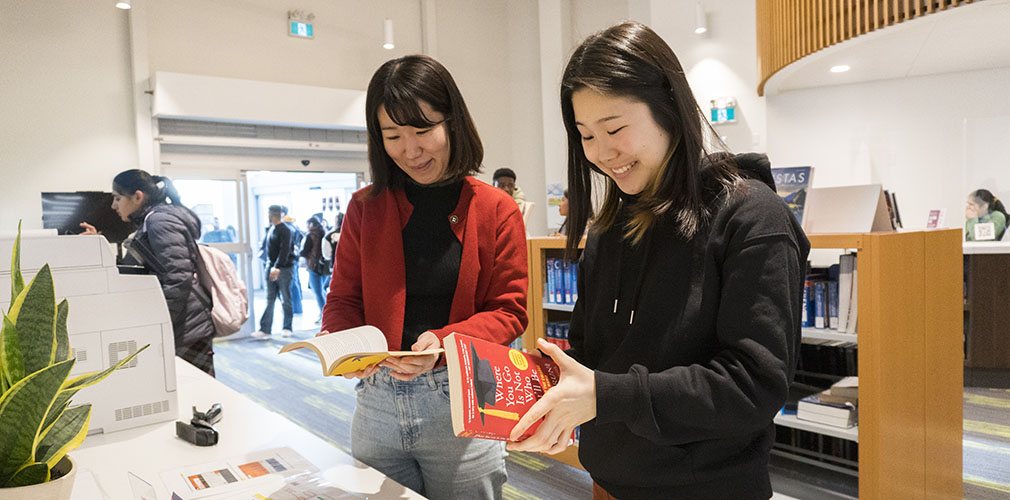 two students reading a book in the library