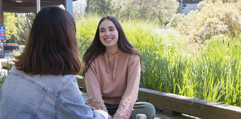 two students sitting and chatting outside